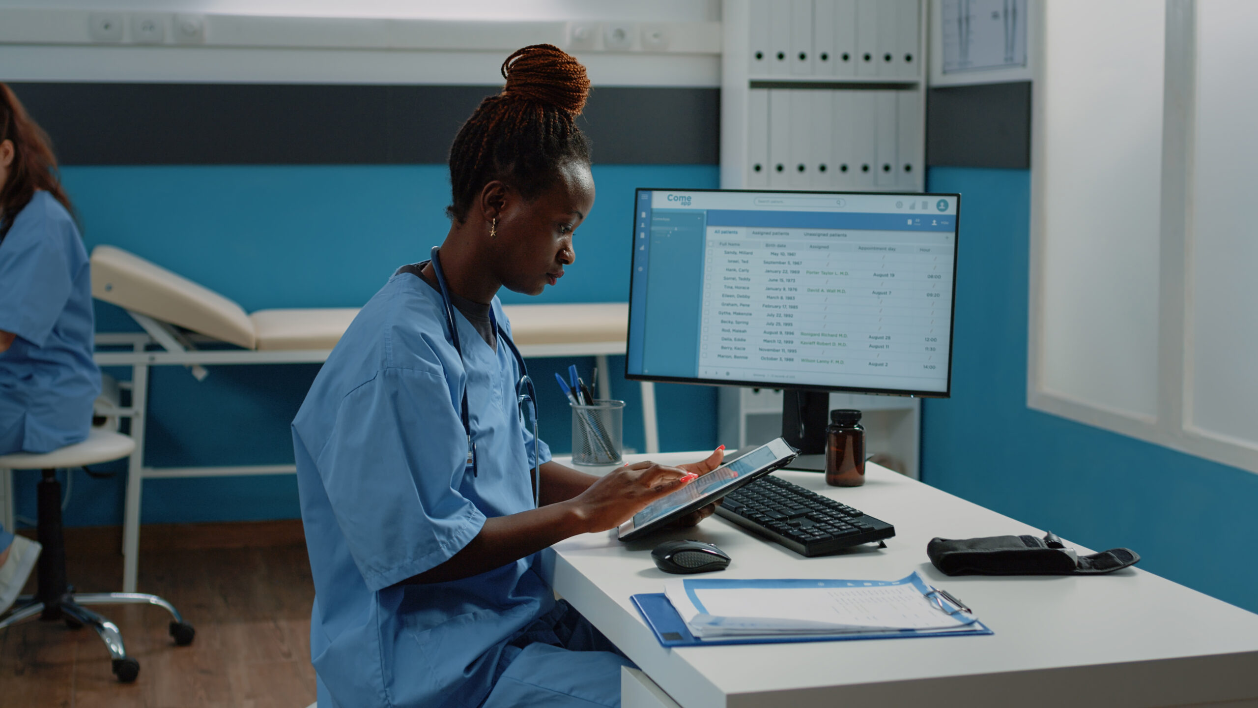African american nurse using digital tablet for treatment. Black medical assistant looking at screen of device while wearing uniform and stethoscope in doctors office for healthcare.